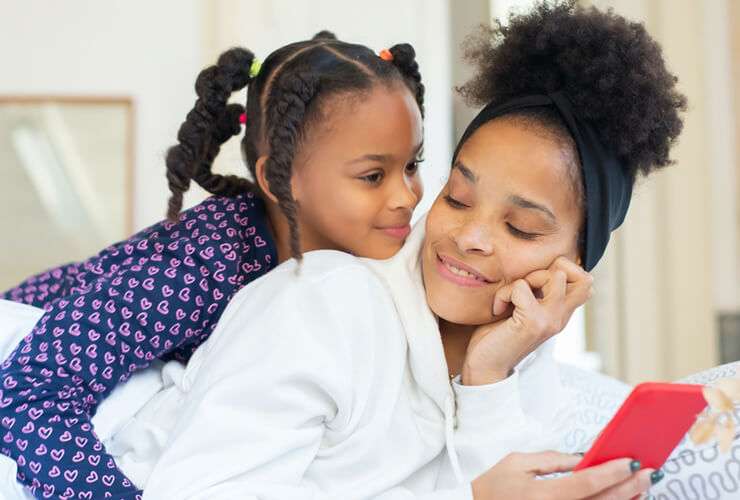 Mom and daughter lie in bed and check a mobile phone together